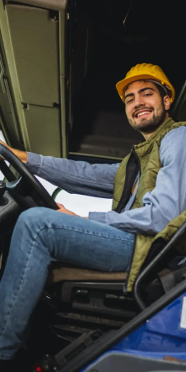 Lächelnder LKW-Fahrer mit gelbem Schutzhelm sitzt am Lenkrad im Führerhaus eines Lastwagens – LKW-Fahrer aus Polen